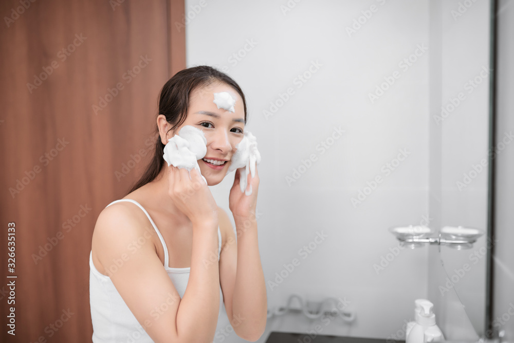 Happy beautiful lady cleaning her face with soap in bathroom
