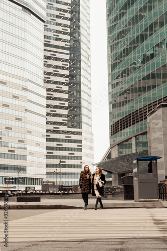 Female friendship, relationships. Two girls are drinking coffee on the street near glass office buildings, a corporation, a bank. The end of the working day of the manager. Coffee on the run.