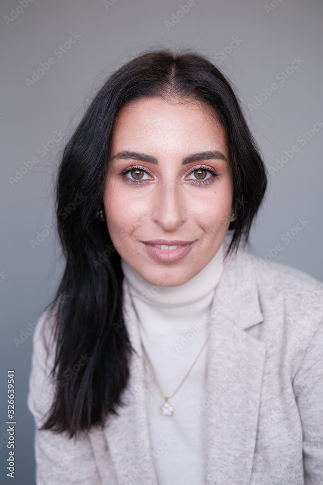 Portrait of a smiling mid-aged business woman in a light milk-colored trouser suit and turtleneck against a light wall. Portrait of a smiling mid-aged business woman in a light milk-colored trouser suit and turtleneck against a light wall.