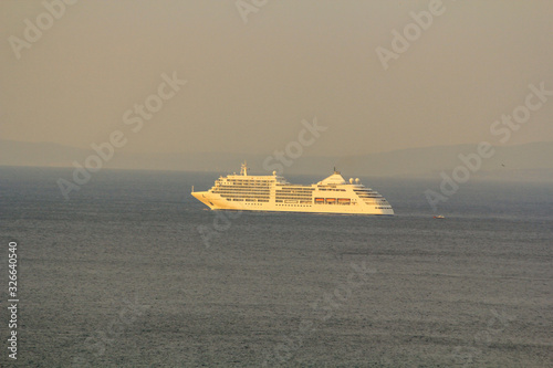 Fototapeta Naklejka Na Ścianę i Meble -  Large cruise ship with sun rays near the coast against the background of mountains