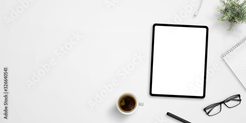 Office desk with tablet mockup and negative space. Cup of coffee, plant, glasses, pen and pad beside. Hero, header image or banner composition