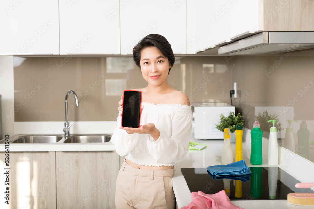 smiling young woman showing blank smartphone screen in kitchen smiling young woman showing blank smartphone screen in kitchen