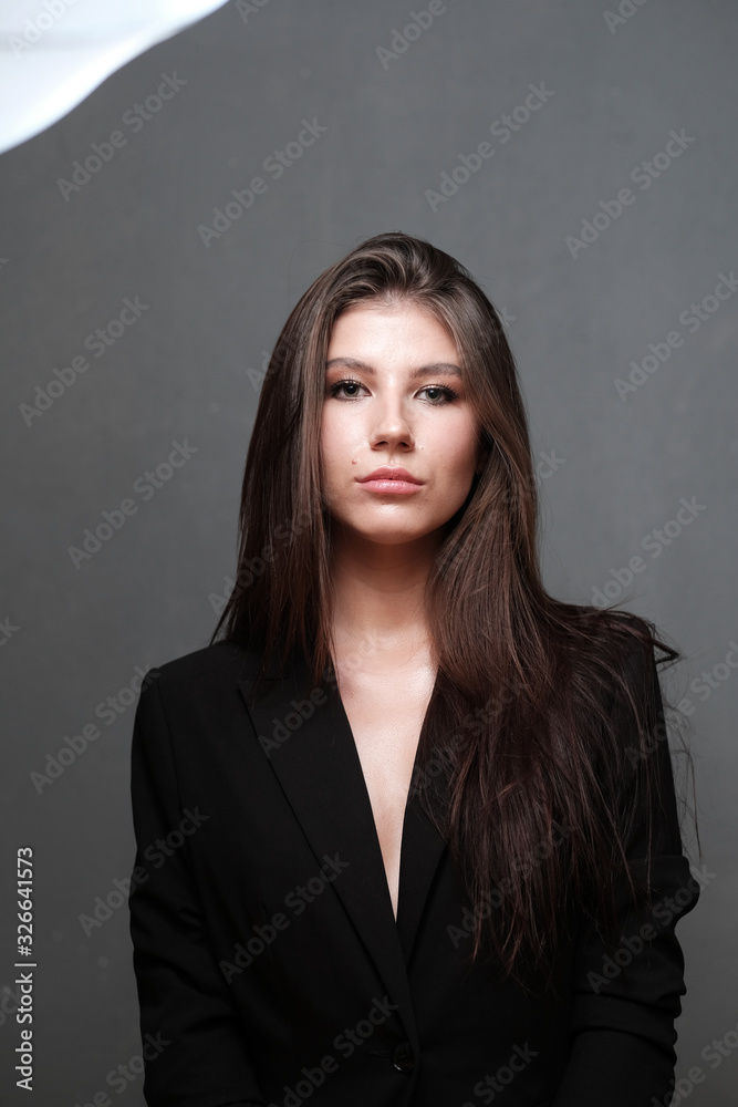 Close-up portrait of a beautiful cute girl with long hair and in a black jacket on a gray background. Girl posing for the photographer in a photo studio. Close-up portrait of a beautiful cute girl with long hair and in a black jacket on a gray background. Girl posing for the photographer in a photo studio.