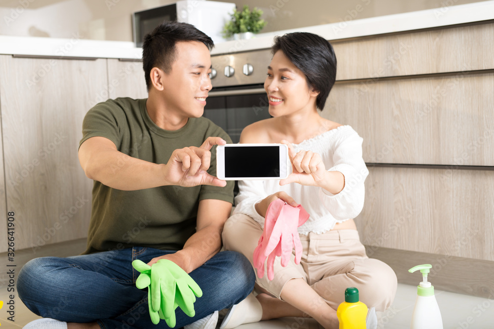 Obraz premium Happy young Asian couple showing smartphone while cleaning house.
