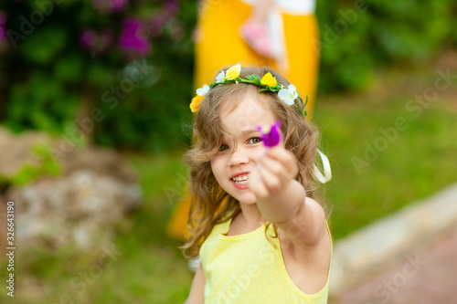 little girl in wreath holds out hand with a flower