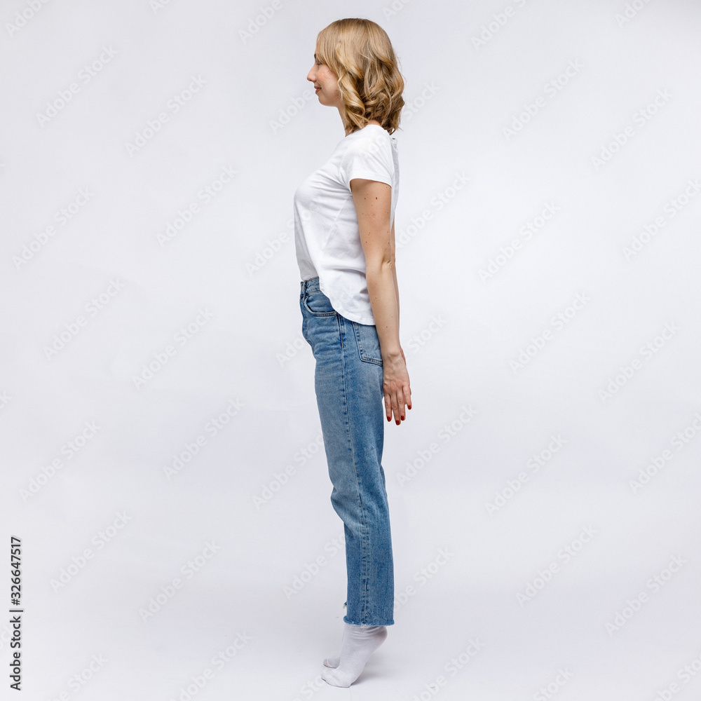 A blonde girl is stands and smiling in a white t-shirt and blue jeans on a white background. A blonde girl is stands and smiling in a white t-shirt and blue jeans on a white background.