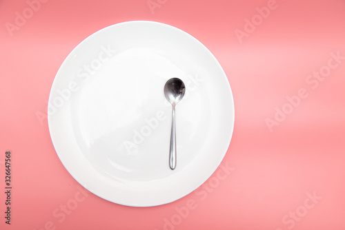 White plate with spoon on a pink background.