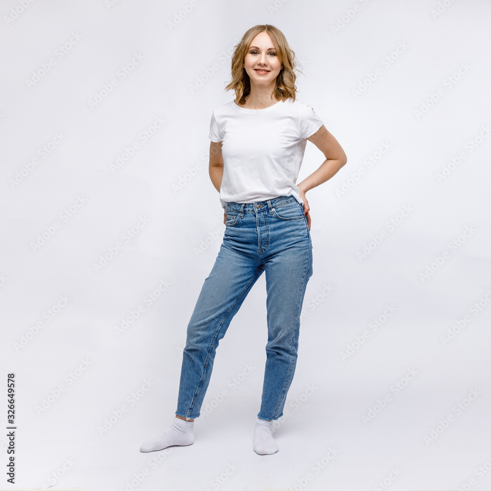 A blonde girl is stands and smiling in a white t-shirt and blue jeans on a white background. A blonde girl is stands and smiling in a white t-shirt and blue jeans on a white background.