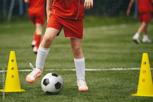 Football soccer kids team exercising with balls. Young athletes during the team training before the match. Young players in red sportswear exercises with ball and yellow cones