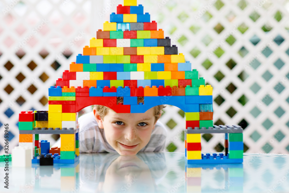 Little blond child playing with lots of colorful plastic blocks ...
