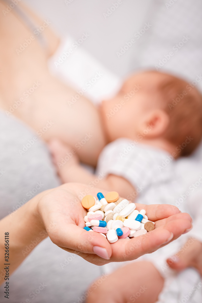 Mother holding handful of medicine while breastfeeding newborn baby Mother holding handful of medicine while breastfeeding newborn baby