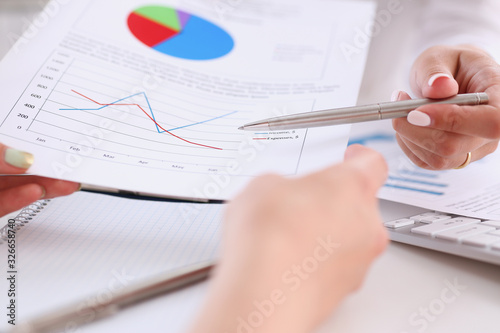 Businesswoman holding a silvery pen in her hand indicates the interlocutor for a digram on the form of annual report on the financing of organizations trains the processing of this statistical study photo