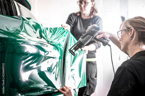 Canvastavla Zwei Frauen folieren ein neues Auto mit grüner Folie