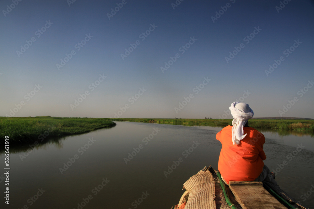 mężczyzna siedzący tyłem na końcu czółna patrzący w dal płynący spokojną rzeką niger w mali - obrazy, fototapety, plakaty 