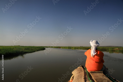 mężczyzna siedzący tyłem na końcu czółna patrzący w dal płynący spokojną rzeką niger w mali © KOLA  STUDIO