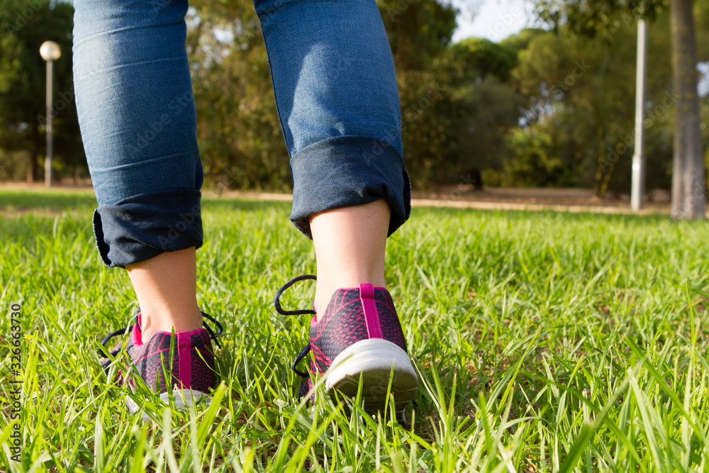 woman in running shoes walking on green and long grass woman in running shoes walking on green and long grass