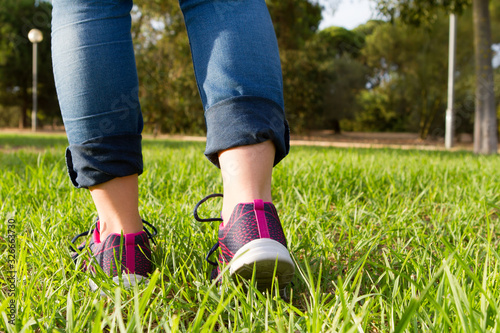woman in running shoes walking on green and long grass