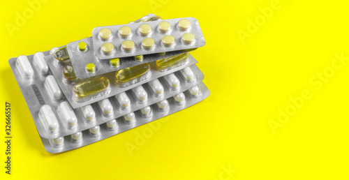 Capsules and pills packed in blisters on yellow background