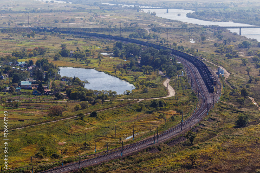 View from above. Beautiful panoramic view of the railway with freight trains passing near the wide river.