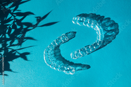 Invisible aligners teeth brackets on blue background with flower shadow