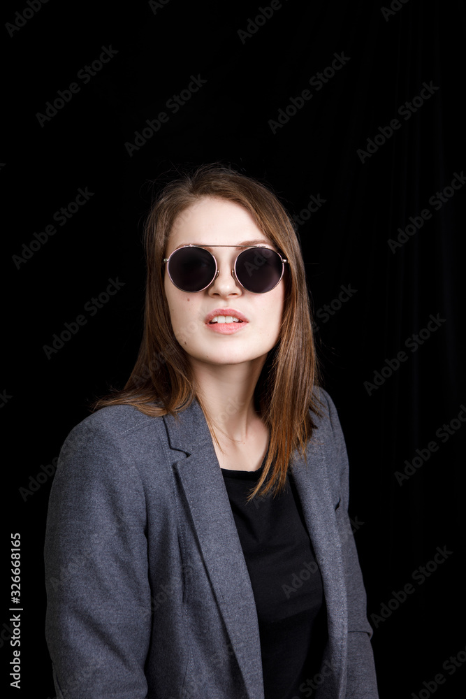 Image of cute confident young lady standing over black background in studio, wearing grey jacket and fashionable eyeglasses, having blond hair Image of cute confident young lady standing over black background in studio, wearing grey jacket and fashionable eyeglasses, having blond hair