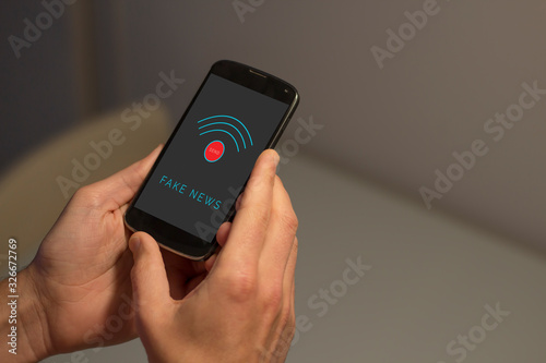Hands holding mobile phone with fake news concept on the screen.