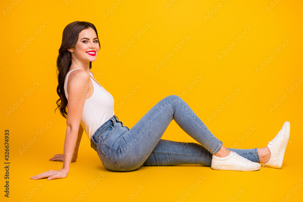 Full body profile photo of funny pretty cheerful lady sit floor cozy dreamy traveler toothy smiling wear white tank-top jeans shoes isolated bright yellow color background