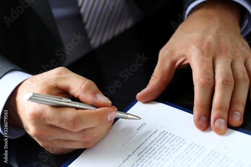 Male arm in suit and tie fill form clipped to pad with silver pen closeup. Sign gesture, read pact, sale agent, bank job, make note, loan credit mortgage investment, finance chief, legal law concept