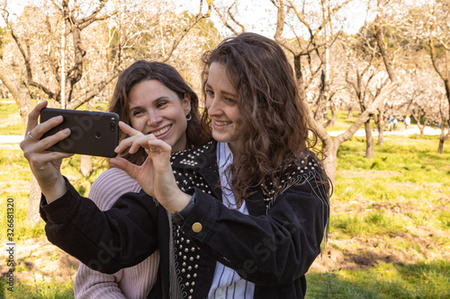 Dos chicas haciéndose selfies en un parque lleno de almendros en flor en un dia primaveral
