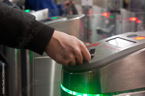 A woman’s hand with a wedding ring on her finger applies a ticket to the yellow circle of an automatic subway system in Moscow. The yellow circle is a sensor of subway access system. Translation: pass