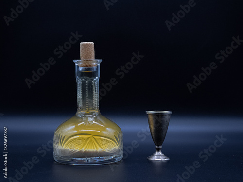 Vintage carafe with homemade vodka and the metal glass on the dark background. Alcoholic drink hrenovuha in transparent vintage bottle and iron shot. photo