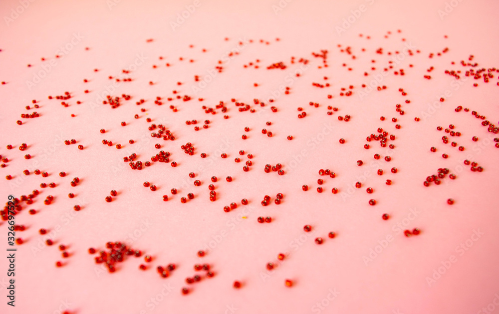 The handful of scattered red beads on a pastel light pink background.
