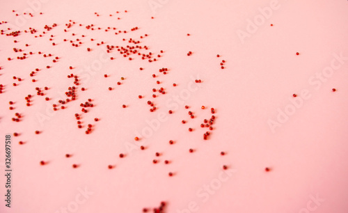 The handful of scattered red beads on a pastel light pink background.