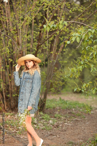  beautiful blonde girl with a bouquet of flowering branches in a straw hat and in a blue jeans jacket in a spring garden where trees bloom © Alina
