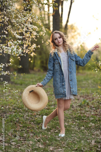 beautiful blonde in a blue denim jacket in a spring garden where trees bloom