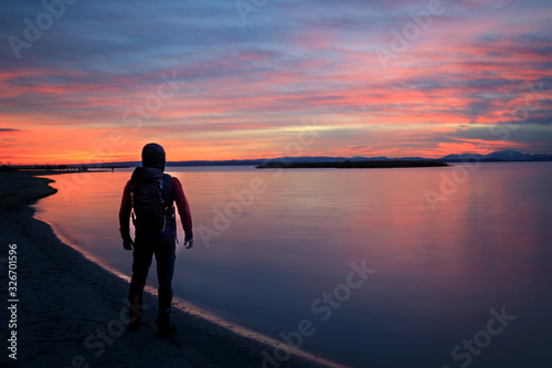 hiker with bagpack standing at lake during sunset