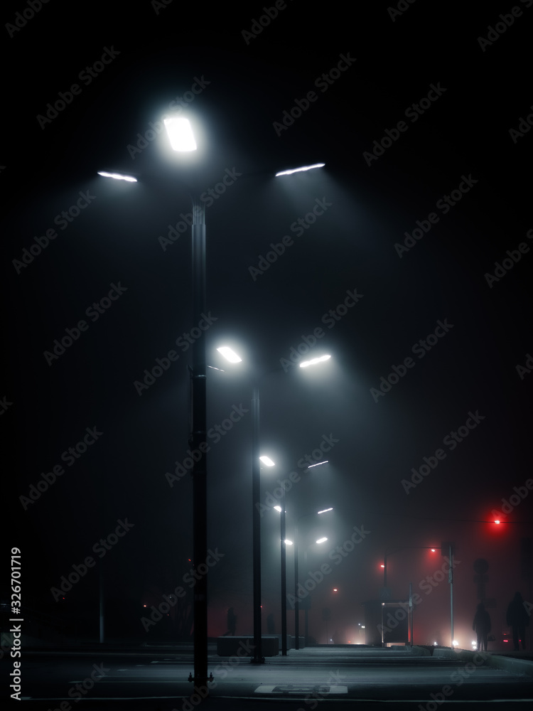 Modern street lights in the fog on empty parking in the night. Cyberpunk style shot. Urban lamp posts against dark sky. Moscow city, Russia.