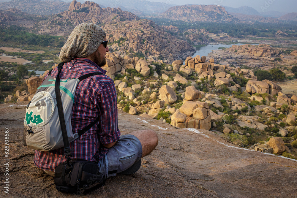 Tourist guy sitting on the edge of a hill. Beautiful view of the amazing Hampi's ruins. Beautiful view of the amazing Hampi's ruins. Karnataka, India