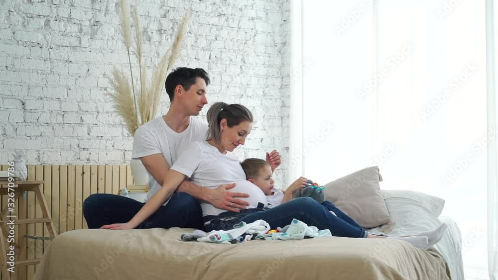 Beautiful Pregnant Woman with her Husband and Little Son Sitting in Bedroom. They are in Expectation of the Birth of a New Baby. Pregnancy, Maternity, Preparation, Expectation and People Concept Beautiful Pregnant Woman with her Husband and Little Son Sitting in Bedroom. They are in Expectation of the Birth of a New Baby. Pregnancy, Maternity, Preparation, Expectation and People Concept