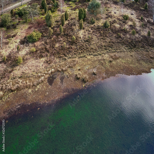 Aerial view from the shore of a lake in the heath  with the heath landscape with heather  juniper  pines  spruces and bushes