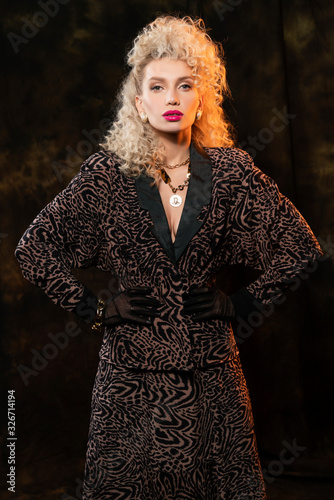 Beautiful blonde girl with elegant hairstyle and big breasts, wearing a leopard print dress and gold jewelry, posing on a vintage fabric background in the eighties style. Trendy advertising design.