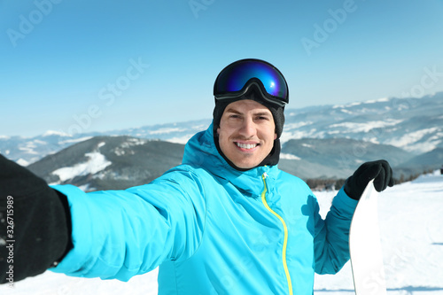 Happy man with snowboard taking selfie in mountains. Winter vacation