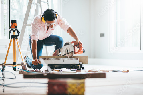 Smart indian contractor hand using sawing machine wood work and working overall equals a wooden bar in the house renovation background. Home improvement ideas concept.