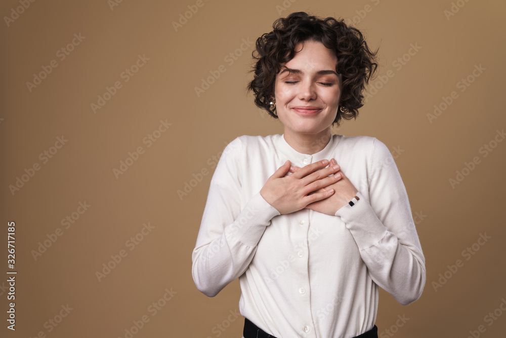 Image of excited beautiful woman smiling and holding hands on her chest Image of excited beautiful woman smiling and holding hands on her chest