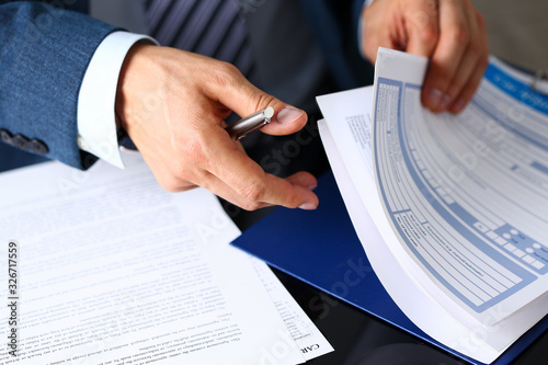 Male arm in suit offer insurance form clipped to pad and silver pen to sign closeup. Strike a bargain, driver money loss prevention, secure road trip, harmless drive idea, owner protective concept photo