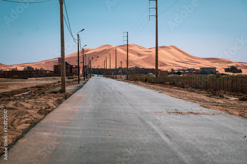 Erg Chebbi, Sahara sand dunes in the background. In foreground, empty, dry road to Merzouga with street poles on the sides, Morocco © Lukasz Machowczyk