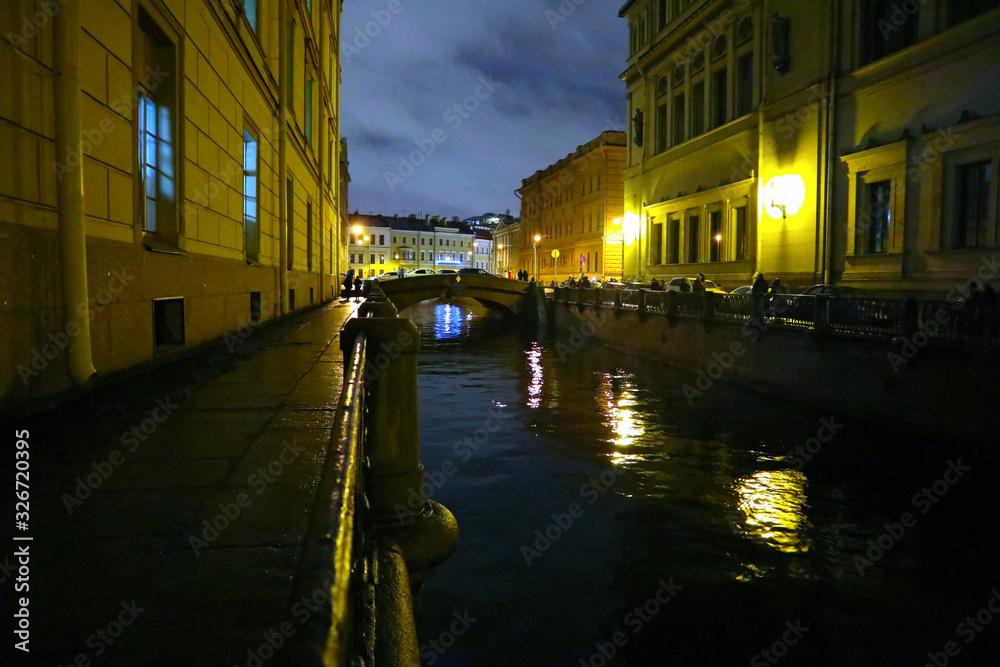 Night city and river in St. Petersburg, Russia. Canal with dark water, a bridge and street in the city center.