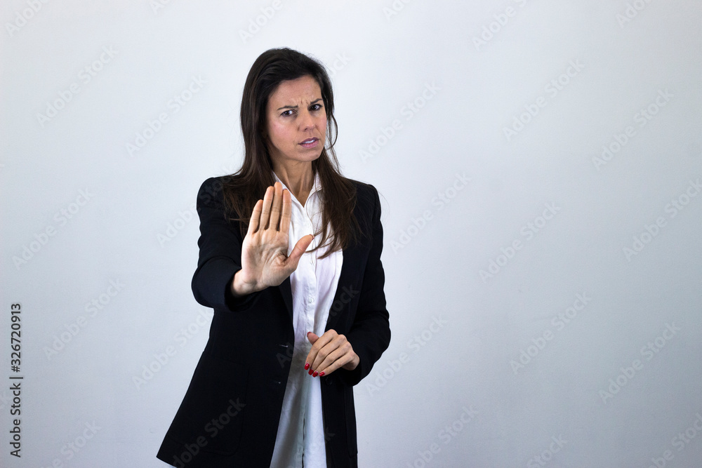 Portrait of attractive caucasian bussiness woman model showing refusal gesture, has seriouss facial expression, isolated on gray background studio shot, white shirt and black jacket, dark air. Place f Portrait of attractive caucasian bussiness woman model showing refusal gesture, has seriouss facial expression, isolated on gray background studio shot, white shirt and black jacket, dark air. Place f