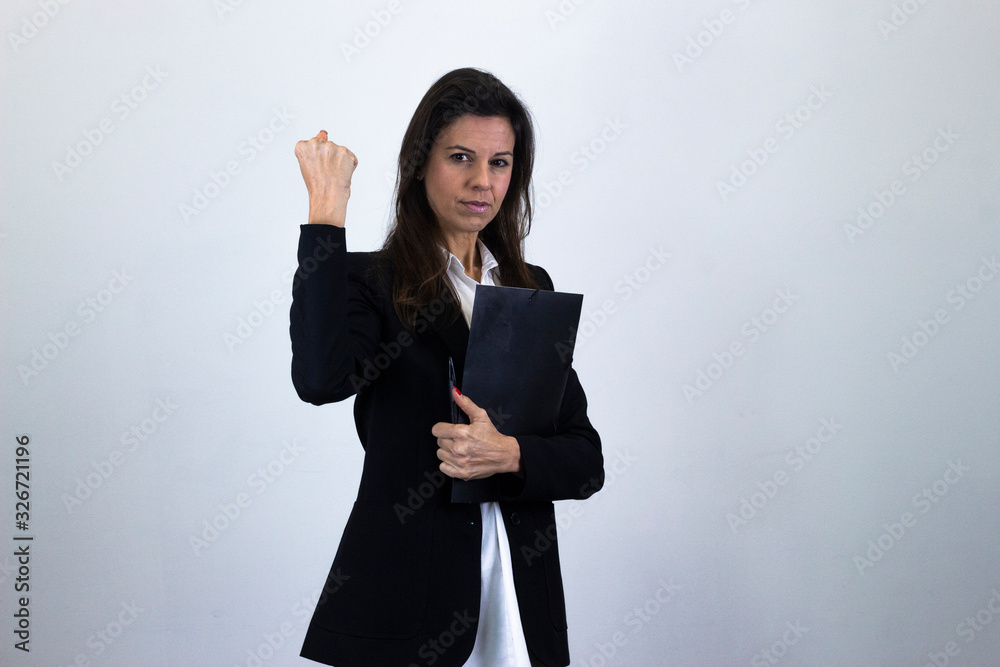 Portrait of bussiness woman model with a folder in her hands showing thumb up gesture, isolated on gray background studio shot, white shirt and black jacket, dark air. Place for your text in copy spac