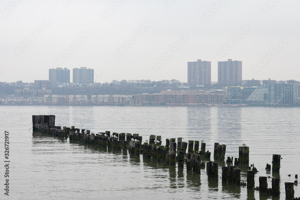 Obraz premium Wood Posts in the Hudson River along the Shore of Lincoln Square New York City with a view of West New York New Jersey during a Foggy Day
